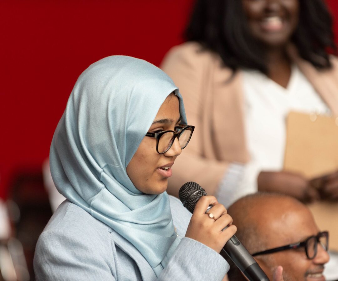 Photo of person speaking into microphone at event.